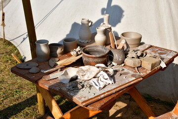 A close up on a wooden table with numerous clay pots, vases, jugs, and mugs scattered around next...