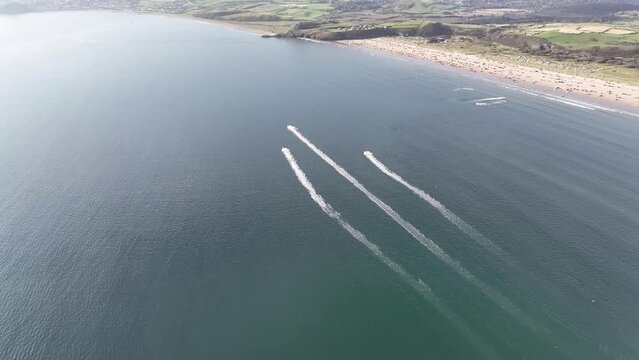 4K 60 FPS aerial drone shot of 3 Jetskis out on the blue sea near a sandy beach coastline on a sunny summers day in Wales, UK. Black Rock Sands, United Kingdom