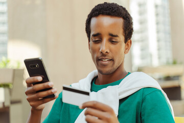 Portrait of attractive African American man holding mobile phone and credit card
