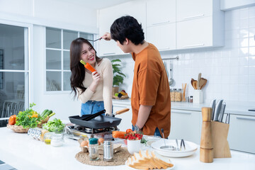 Happy portrait of loving young asian of having fun standing a cheerful preparing food and enjoy cook cooking with vegetables, meat, bread while standing on a kitchen Condo life or home