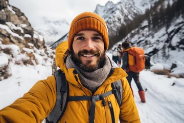 Tafelkleed A smiling young hiker man taking a selfie in the snowy mountains. Winter travel and outdoor activities concepts. © Nanci