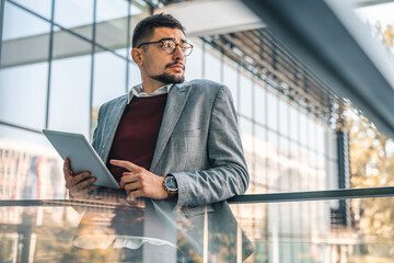 Serious young smart looking businessman using digital tablet outside of modern building. Male...