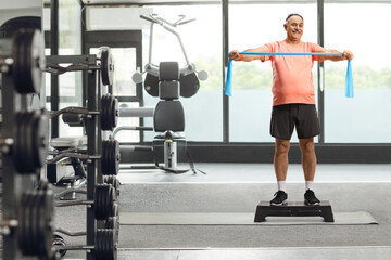 Mature man in sportswear exercising with a stretch band on a step aerobic platform