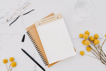 Flat lay of white notebook with copy space for text, glasses and yellow flowers on white marble background