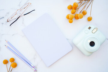 Flat lay of white marble table with stationery, glasses, yellow flowers and photo camera