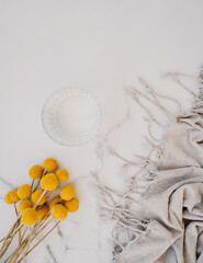 Glass of water, grey plaid and yellow flowers on white marble background.