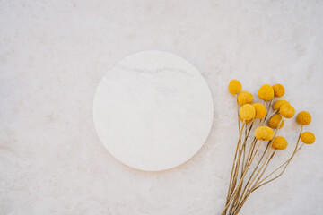 White marble cosmetic podium product design and bouquet of dry yellow flowers on white marble background