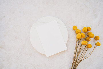 White card on white podium and bouquet of dry yellow flowers on white marble background