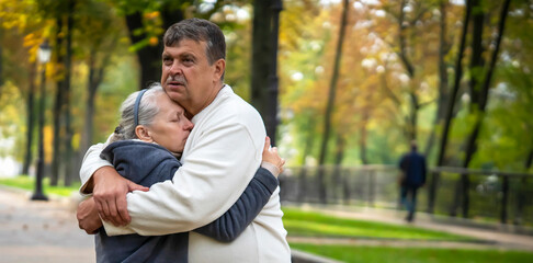 An elderly couple hugs in the park during the walk.