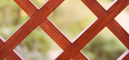 Wooden lattice, a decorative fence with garden on the background.