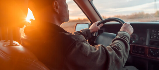 A man is driving his car on the road at sunset.