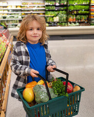 Child with shopping basket full of vegetables and fruits. Kid in a food store. Supermarket shopping and grocery shop concept. Child with shopping basket. - obrazy, fototapety, plakaty
