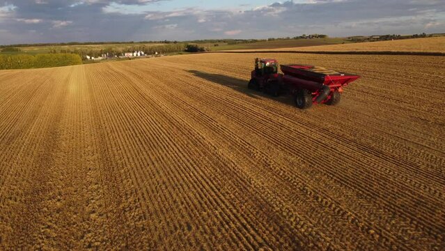 Tractor pulling a full grain cart across field stubble during harvest in North America.
