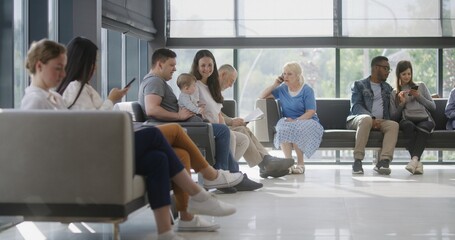 Diverse multicultural people sit on couches in clinic lobby area, wait for appointment with doctor...
