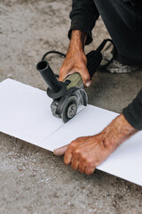 A man, a worker in an outdoor workshop, cuts off a plastic white material for insulation with a grinder, an electric cutter. Photography, industry.