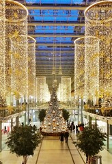 A towering Christmas tree, adorned with twinkling lights and ornaments, stands proudly in the center of a bustling mall