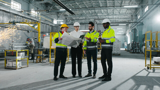 Group of industrial heavy engineers wearing in protective helmets and yellow vests walking at background of workprocess. Multicultural employees working and cooperate at construction site.