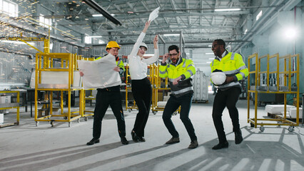 Multicultural engineers dancing at modern manufacturing factory and clapping hands. Employees in...