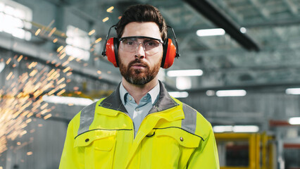 Industrial engineer in protective headphones wearing safety vest works in heavy manufacturing...