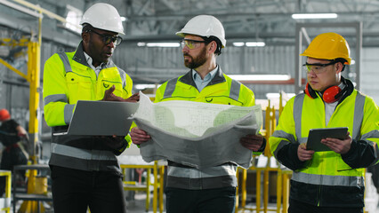 Male industrial engineers communicate with each other. Factory workers using gadgets and blueprint...