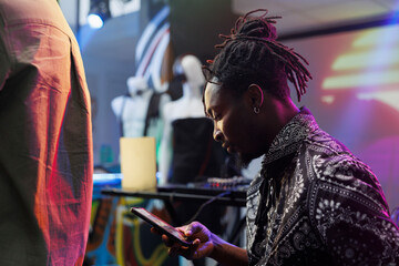 Young african american man using smartphone while resting in nightclub. Clubber scrolling social...
