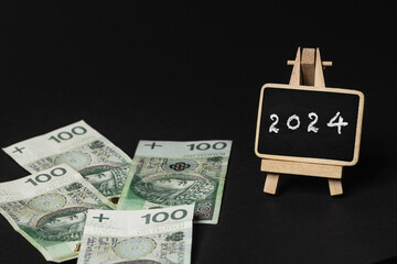 scattered Polish money on a black background, next to it there is a writing board with the inscription "2024" (selective focus)