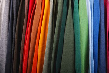 Warm sweaters. Autumn, winter clothes. Metal rack with various sweaters on hangers placed in modern...