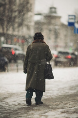 Blured figure of old woman in warm clothes walking in the street in white snowy winter day. First...