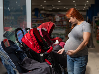 Red-haired pregnant woman chooses a stroller in a children's store. 