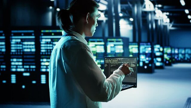 Qualified IT developer running code on laptop, troubleshooting and upgrading data center equipment designed to accommodate server cabinets, networking systems and storage arrays