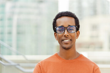 Fototapeta premium Portrait of attractive smiling African American man wearing eyeglasses, casual clothes looking at camera outdoors. Handsome businessman on urban street. Vision concept