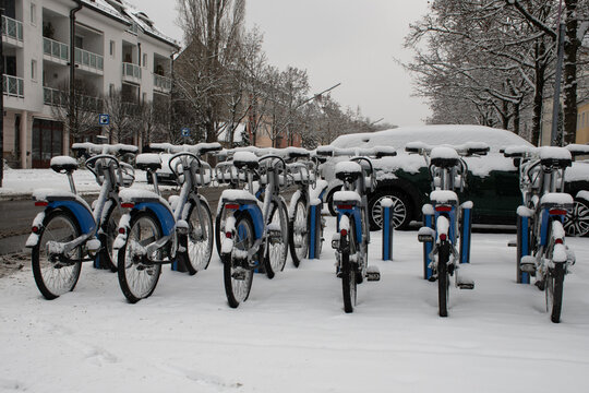Munich, Germany - January 6, 2021: Snow-covered shared bikes by MVG, a public transport operator, parked at a bike stand outside a subway station in winter.