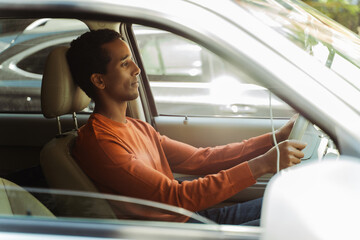 Smiling handsome African American man wearing stylish casual clothes driving car, looking at road. Transportation, road trip, car sharing concept