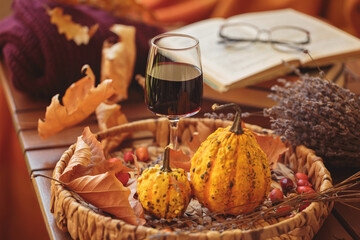 Glass of red wine on wooden table decorated with pumpkins, books and dried leaves outdoor. Autumn...