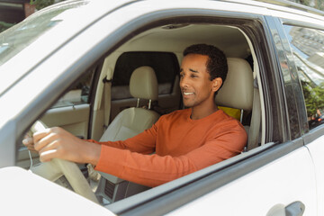 Handsome smiling African American man wearing stylish casual clothes driving new car. Transportation concept
