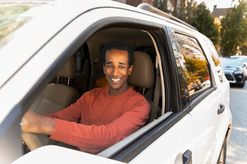 Portrait of young smiling African American driver in casual clothes sitting behind wheel, driving, looking in rear view mirror. Concept of movement, vehicle