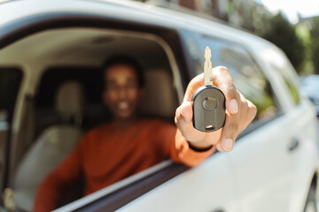 Selective focus, closeup, African American man sitting in car behind wheel showing car key....