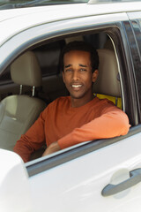 Portrait of young positive African American driver in casual clothes sitting behind wheel, driving car, looking at camera, closeup. Transportation concept