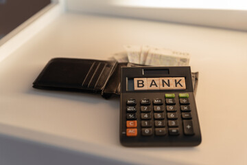A wallet with banknotes lying next to a calculator with a Bank sign. The concept of spending during a recessionary crisis.