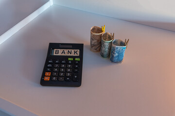 Banknotes stacked in a roll of 3 denominations of 50 zloty 100 and 200 zloty next to which lies the Bank's wood sign on a calculator. The concept of spending during the recession crisis. 