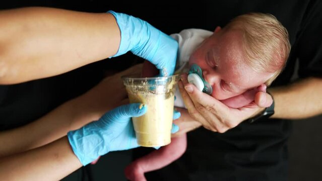 Making a model of newborn's hand. Little kid is sleeping in dad's hands and his hand is deepened into the mixture.