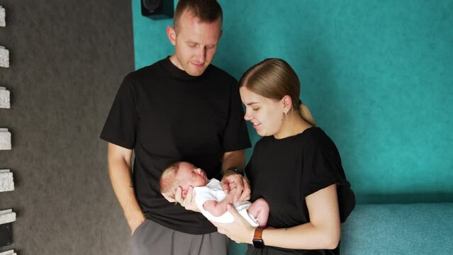 Beautiful Caucasian couple with newborn. Parents in black t-shirts waving their little baby.