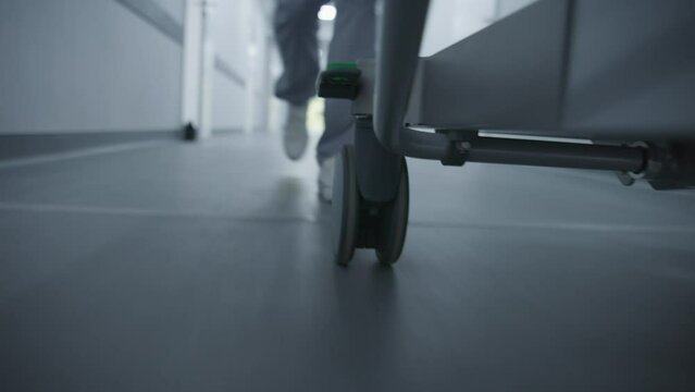 Doctor or paramedic runs and pushes gurney with seriously injured patient towards surgery room. Medic save human life. Close up of medical staff legs. Bright hospital corridor. Emergency department.