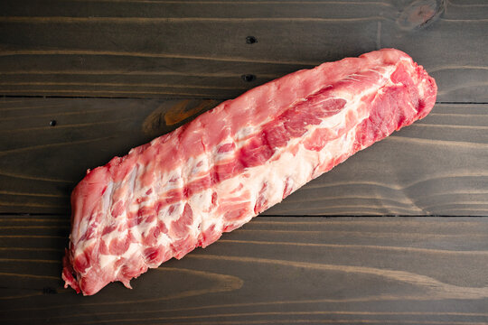 Raw Rack of Baby Back Ribs on a Wooden Table: An uncooked rack of pork loin ribs viewed from directly above