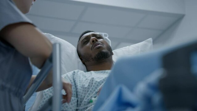 African American man lies on stretcher and talks with doctors before surgery. Physician stands near gurney and calms patient in medical center. Medical staff work in emergency department. Close up.