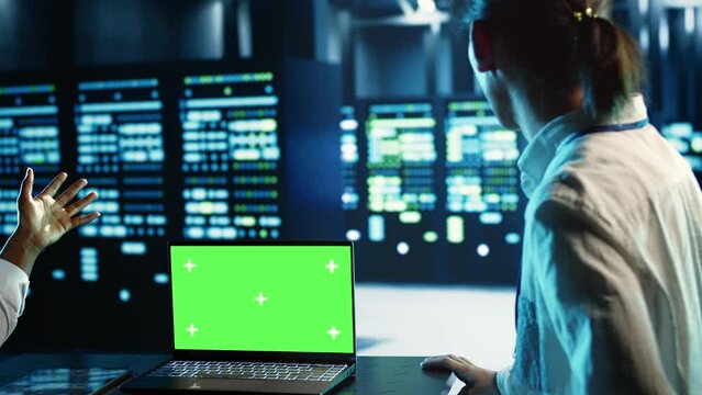 Engineering coworkers using mockup laptop to implement artificial intelligence parallel processing. Adept colleagues work on green screen device, enabling AI systems to process machine learning data