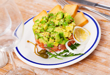 Popular dish of French cuisine is salmon tartar with avocado, served with a slice of lemon and...