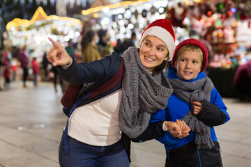 Portrait of smiling cute preteen boy walking with his mother at colorful Christmas street market. Happy family moments