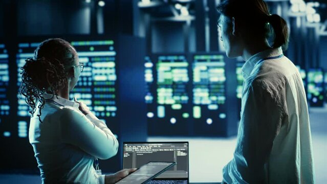 Technicians programming in server room housing advanced infrastructure storing massive datasets. Workers running code on laptop to upgrade data center racks doing complex computational operations