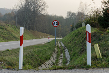 Droga, biało-czerwone słupki, znak ograniczenia prędkości. - obrazy, fototapety, plakaty